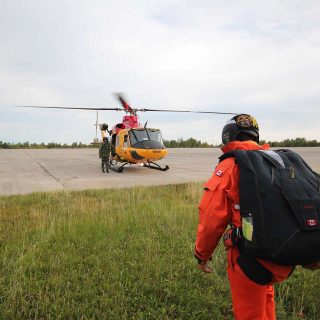 Canadian military jumper wearing a large skydiving rig walking toward a helicopter for search and rescue training