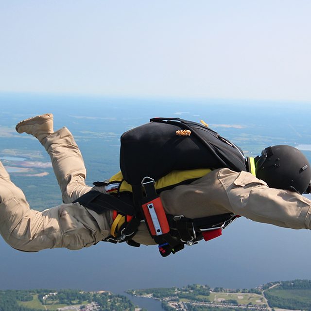 A jumper in tan fatigues in freefall wearing modern military training parachuting equipment