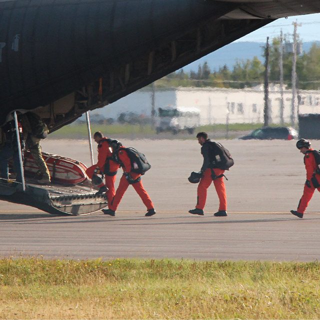 Military skydivers in red jumpsuits boarding a C-130 wearing rigs and equipment developed and sold by Mobility Lab Inc.
