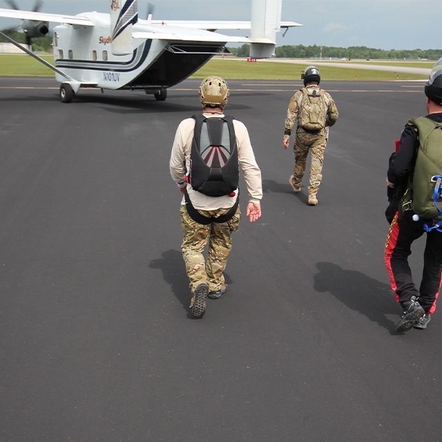 Three men wearing modern military equipment walk to board a tailgate aircraft at Mobility Lab Inc
